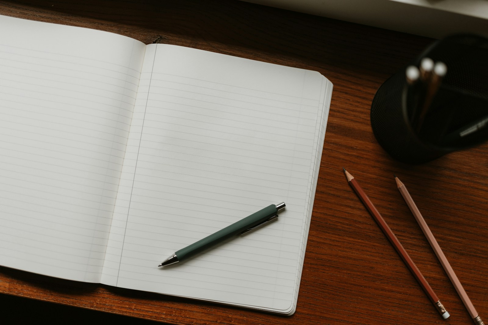 Een open notitieboek met een pen en potloden op een houten bureau.